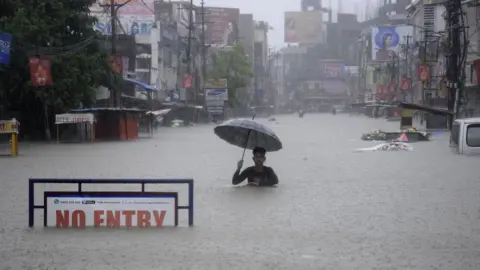 Getty Images An Indian man holding an umbrella struggles along a flooded street in Agartala, Tripura.