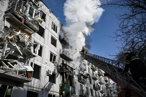 AFP Firefighters work on a fire on a building after bombings on the eastern Ukraine town of Chuguiv on 24 February 2022