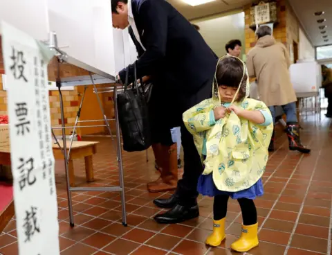 Reuters A girl stands next to her father filling out his ballot for a national election at a polling station in Tokyo, Japan October 22, 2017