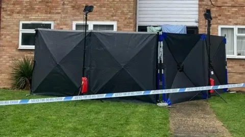 Lewis Adams/BBC Shot of police tent in front of the door