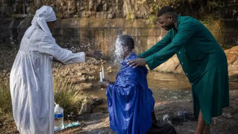 Michele Spatari/AFP Woman pouring milk on another woman and a man holds her shoulder as part of a church ritual, 10 September.