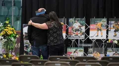 AFP/Getty Images A man is comforted as he looks at photographs prior to a vigil at the Elgar Petersen Arena, home of the Humboldt Broncos