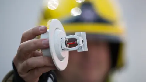 Aaron Chown Technical Fire Safety Officer holding up a sprinkler