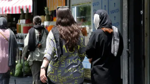 Getty Images Two women walk down a street in Iran without their hair covered