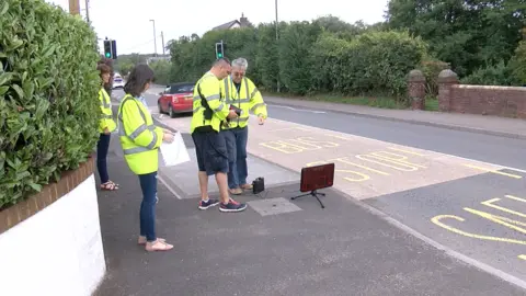 A group of Speed Watch volunteers setting up a light-up speed sign by the road