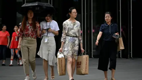 Getty Images A woman, carrying two shopping bags, walks out of a mall in Beijing on August 14, 2019