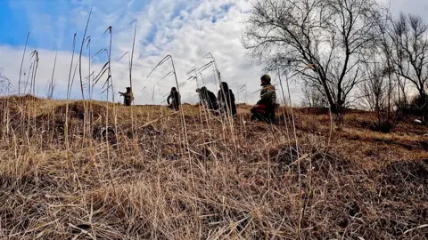 Stu Holland/ BBC Soldiers move through the tall grass