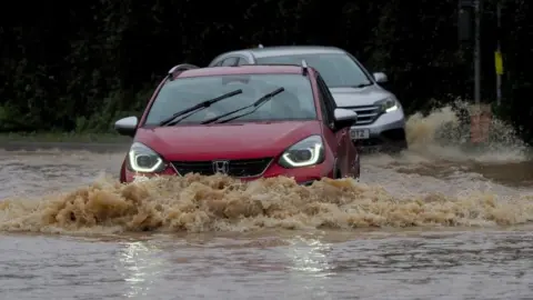 PA Media Vehicles are driven through a flooded road