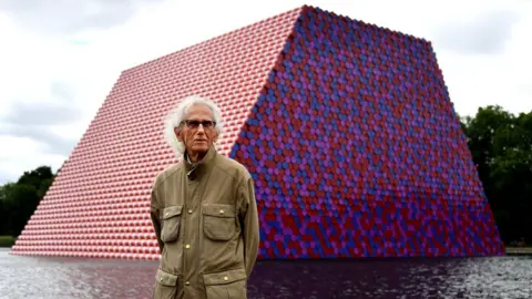 EPA Bulgarian artist Christo stands in front of his artwork Mastaba, built on the Serpentine lake in London, 18 June 2018