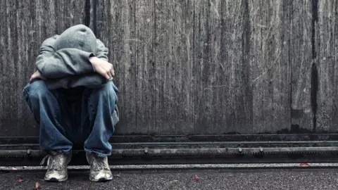 nkbimages Young person crouched up against a wall