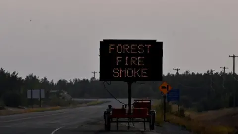 Reuters A helicopter carrying a water bucket passes a sign that reads Forest Fire Smoke as wildfires threatened the Northwest Territories town of Yellowknife, Canada