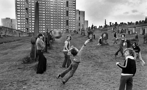 John Sturrock/Report Digital Children playing football, Sighthill Cemetery, Glasgow. Playing amoung the gravestones with high rise tower blocks behind, August 10, 1980