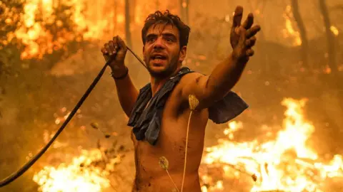 A local resident gestures as he holds an empty water hose during an attempt to extinguish forest fires approaching the village of Pefki on Evia island, Greece, on 8 August 2021