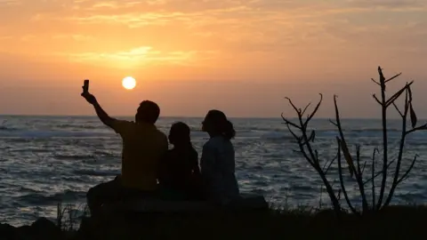 LAKRUWAN WANNIARACHCHI/AFP/Getty Images A Sri Lankan family takes a selfie at sunset on a beach in Colombo