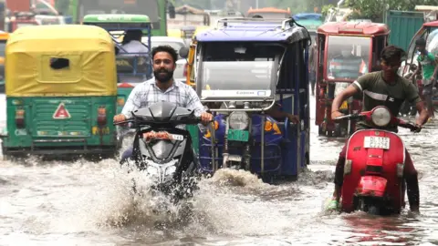 Getty Images Motorcyclists ride through a flooded street after heavy rainfall at Jahangirpuri area in New Delhi in August 2021.