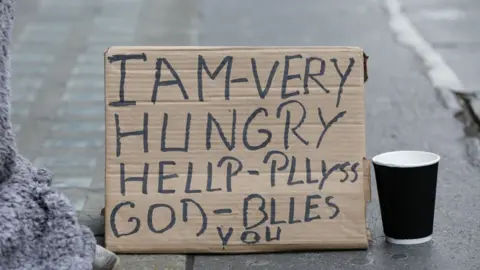 Anadolu Agency/Getty Images A sign reads: "I AM - VERY HUNGRY - HELP PLLYSS GOD BLESS YOU"