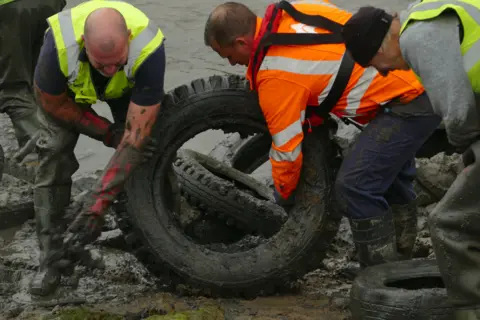 Keep Wales Tidy Volunteers wheeling a tyre out of the muddy river