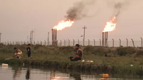 BBC Men fish by oil field with gas flaring in the background