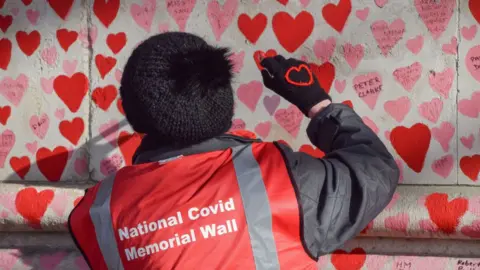 Getty Images A volunteer paints red hearts on the National Covid Memorial Wall in Westminster