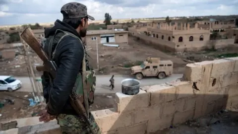 AFP A member of the Syrian Defence Forces stands guard on top of a building in the frontline Syrian village of Baghuz, on 17 February 2019.