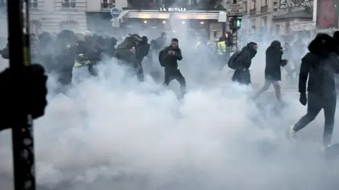 Getty Images Protesters run away from tear gas during a demonstration in Paris, on January 11, 2020