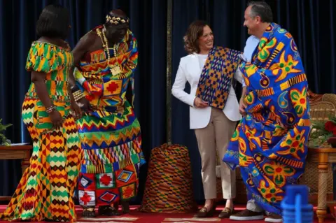 AFP Chief Osabarima Kwesi Atta II (L) looks on (2nd L) looks on as US Vice President Kamala Harris (2nd R) and Second Gentleman Douglas Emhoff (R) react after receiving traditional Kente cloths at the Emintsimadze Palace in Cape Coast, Ghana.