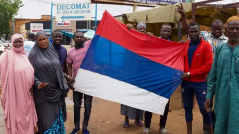 Getty Images Coup supporters unfurl a Russian flag as they take to the streets after the army seized power in Niamey, Niger