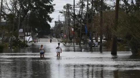 AFP via Getty Images People walk through flood waters in Norco, Louisiana, on August 30, 2021 after Hurricane Ida made landfal