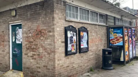 Cheltenham Borough Council The outside of the toilet block showing walls with graffiti on and noticeboards