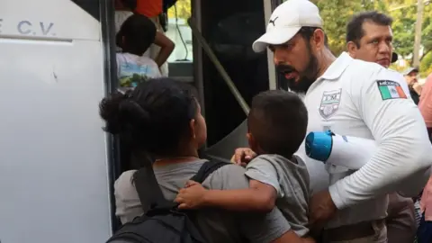 EPA A migrant holding her son talks with an official from the National Migration Institute (INM) before boarding a bus, after finishing a migrant caravan heading to the United States, in the municipality of Mapastepec, state of Chiapas, Mexico, 02 January 2024