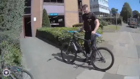 Northamptonshire Police Police officer standing with a bicycle outside a multi-storey car park