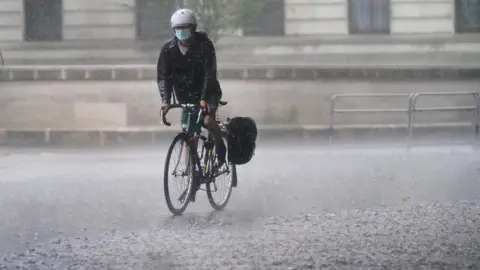 PA Media A cyclist rides through flood water in Horse Guards Road in central London