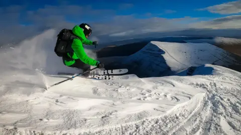 Chris Morris Chris skiing fast through the snow with a snow covered mountain peak in the distance