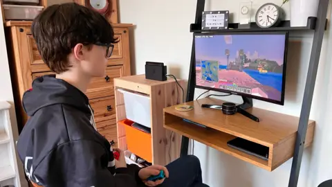 Martin Giles/BBC Michael holding a Nintendon Switch controller and looking at a game on a monitor