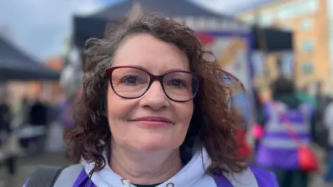 A woman wearing glasses smiles at camera as she attends march in Belfast on International Women's Day