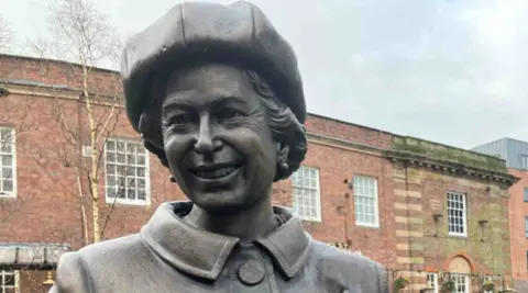 The statue is in the middle of the photo. Buildings are in the background.