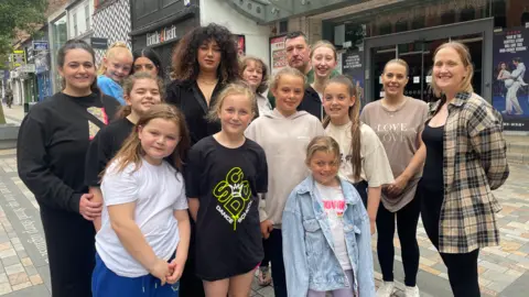 BBC A group of children and adults from a dance group stood outside a theatre in Hanley