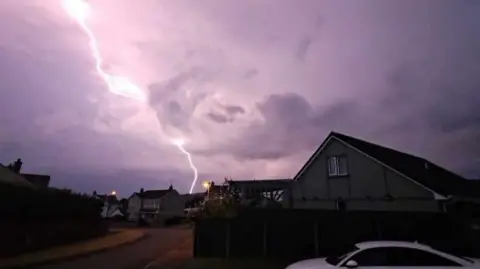 Claire Shannon Shows a bolt of lightning with houses in the foreground