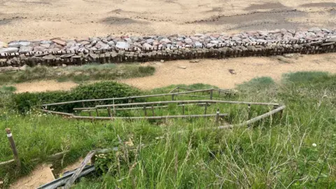 Owen Sennitt/BBC Looking down towards the beach, a series of steps with broken wooden handrails can be seen, with sea defences and sand also visible in the distance