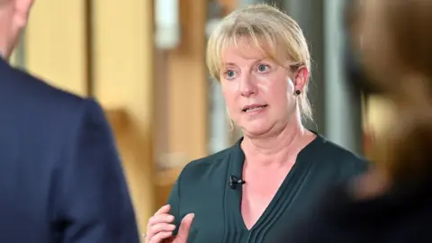 Getty Images Shona Robison, wearing a dark green top, speaks to journalists in the Scottish Parliament 