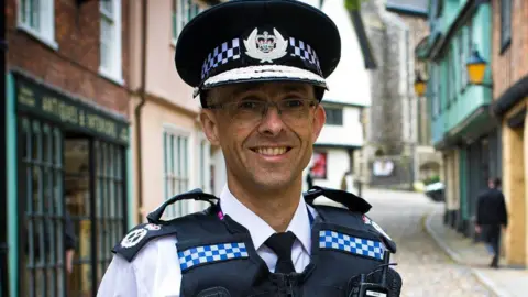 Norfolk Police Chief Constable Paul Sanford in uniform, standing in a Norfolk street, smiling and looking straight to the camera 