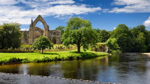 Scene at Bolton Abbey with the winding River Wharfe and stepping stones in foreground and the ruins of the 12th Century abbey in the background