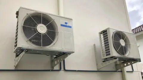 Getty Images Two heat pumps on a cream wall. 
They are cream and 2m a part from each other with large circular extractors. 