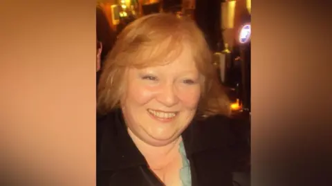 Family handout A smiling woman in a pub or restaurant setting. She is wearing a black cardigan and a blue top