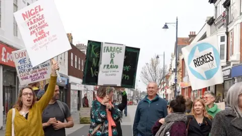 Qays Najm/BBC Protesters holding up anti-Reform UK signs in the street.
