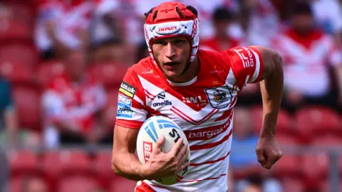 Harry Robertson, wearing St Helens' red and white jersey, runs with a rugby league ball in his right hand