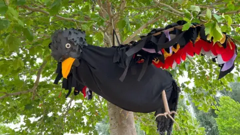 A blackbird made of cloth and other materials hangs from a tree.