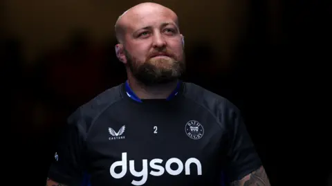 Bath Rugby player Tom Dunn walking out to warm-up for a Prem Rugby match wearing a dark blue rugby shirt.