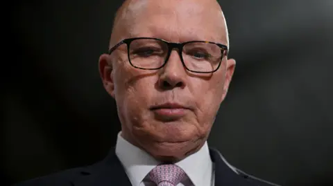 Getty Images Opposition Leader Peter Dutton looks down during a press conference in the electorate of Tangney and suburb of Myaree on May 02, 2025 in Perth, Australia. He is only visible neck up and is wearing a white shirt, black blazer and pale pink tie with a print on it.