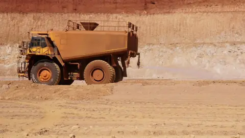 Zoe Corbyn Henry - a truck with a water tank on the back - sprays water on dirt roads.